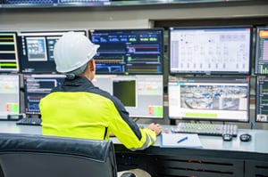 A person wearing a hard hat looking at multiple computer monitors.