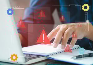 A hand hovering over a notebook and laptop with gear icons.